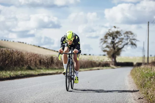 A cyclist riding in an aerodynamic position on a country road